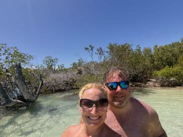A cheerful couple poses for a selfie in shallow waters surrounded by mangroves, capturing a memorable moment during their beach adventure.