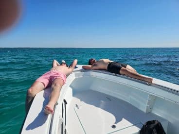 Two friends relax on the bow of a boat, soaking up the sun and enjoying the beautiful turquoise waters — a perfect day for leisure on the water.