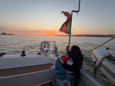 A family enjoys a beautiful sunset on a boat, capturing the moment with a phone — perfect for memorable experiences on the water.