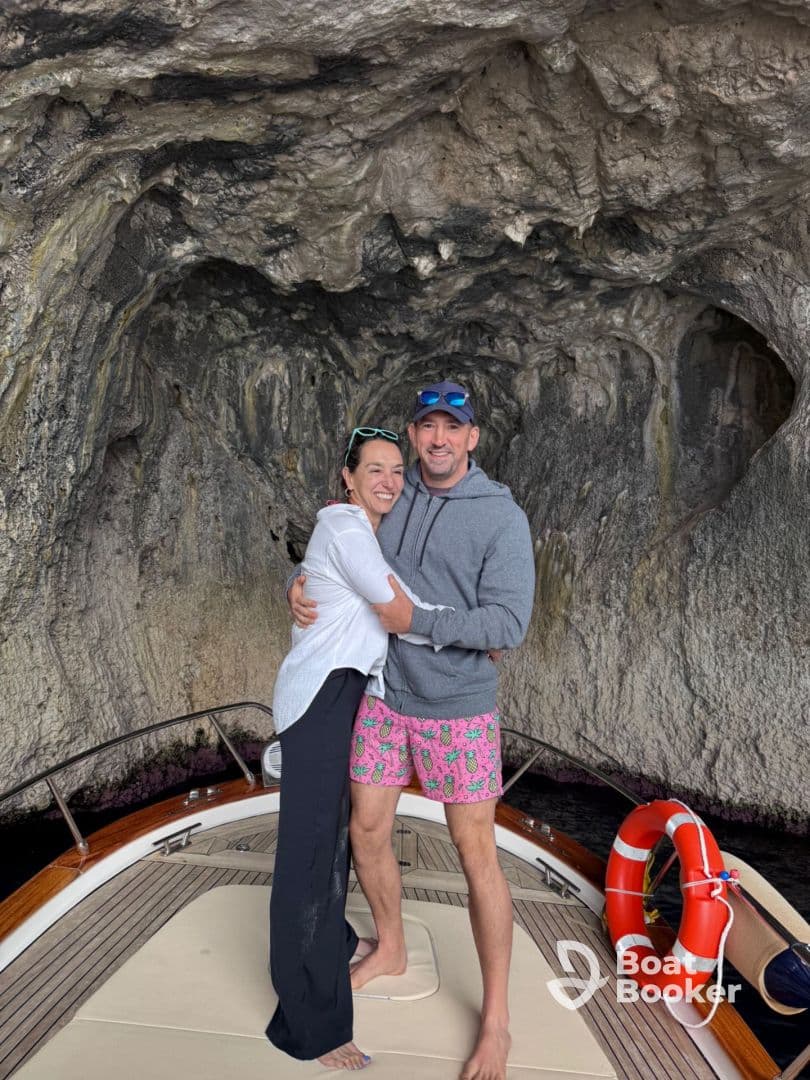 A couple embraces on the deck of a boat inside a stunning cave, capturing a memorable moment during their adventure on the water.