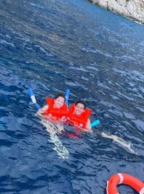 A joyful couple enjoys snorkeling in crystal-clear waters, wearing life jackets for safety — a perfect adventure for water lovers.