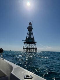 A stunning view of a lighthouse standing tall against a bright blue sky, captured from a boat on shimmering waters — a perfect representation of coastal beauty.