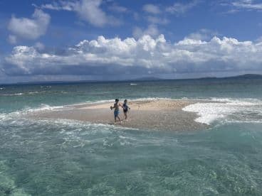 Two children enjoy a playful moment on a sandy sandbar surrounded by clear turquoise waters, perfect for family beach outings and adventures.