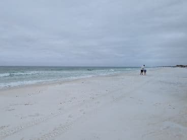 A family strolls along a serene beach, enjoying the tranquil ocean views and soft white sand — a perfect moment for relaxation and connection.
