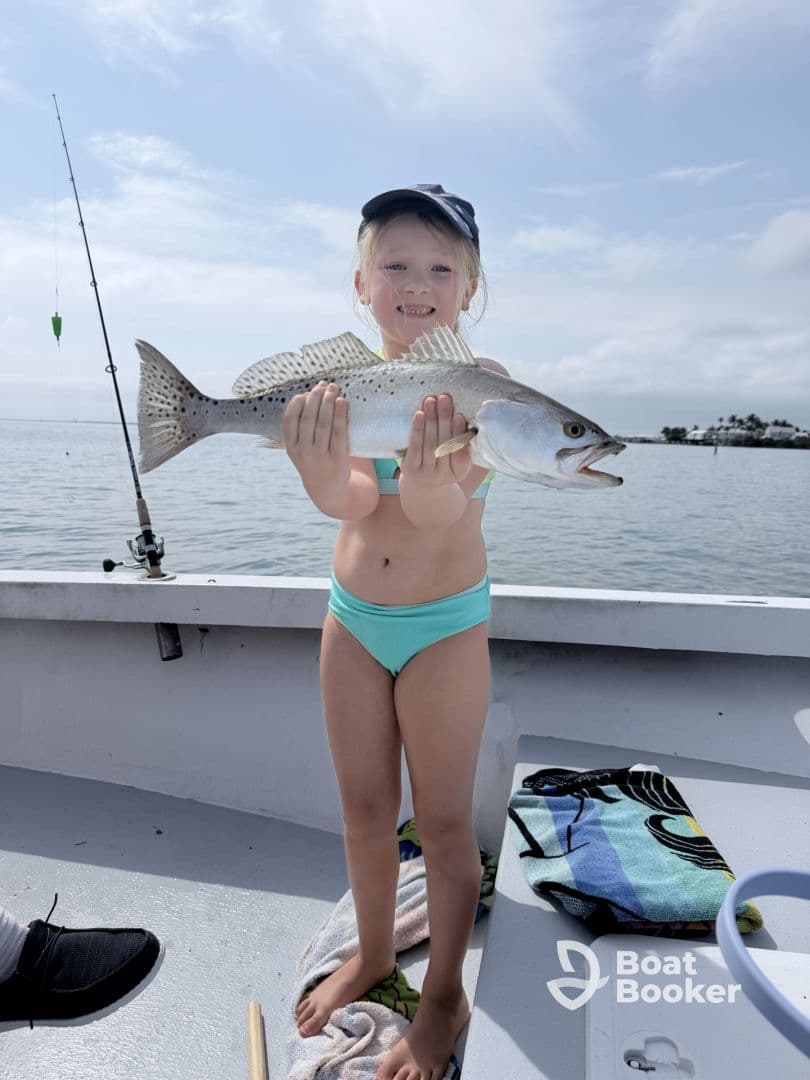 A young girl proudly holds up her catch while fishing on a boat, showcasing the joy of a successful fishing trip.