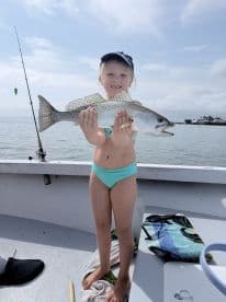 A young girl proudly holds up her catch while fishing on a boat, showcasing the joy of a successful fishing trip.