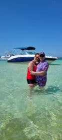 A joyful couple embraces in shallow water with a boat in the background, capturing a perfect moment of celebration and fun under the sun.