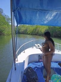A woman enjoys a scenic view while exploring a tranquil waterway surrounded by lush mangroves from the deck of a boat.