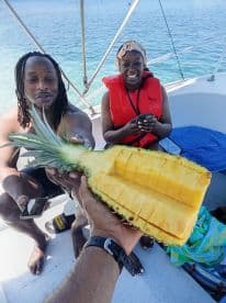 A joyful moment on a boat as friends share a freshly cut pineapple, perfect for enjoying snacks while soaking up the sun on the water.