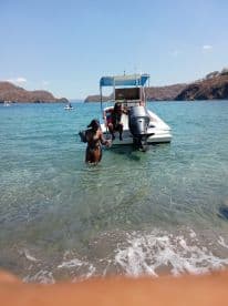 Two individuals enjoy a sunny day at the beach, interacting near a boat in clear waters — a perfect scene for summer adventures and water activities.