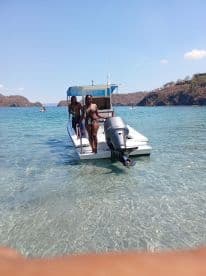 A couple enjoys a sunny day by the water, posing on their boat in clear, shallow waters — perfect for a fun beach outing.