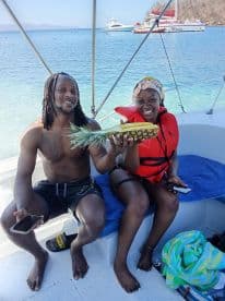 A joyful couple poses with a pineapple on a boat, showcasing a fun moment during their tropical adventure — perfect for memorable celebrations on the water.