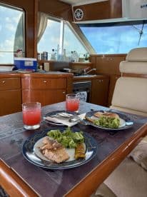 A beautifully set dining area inside a boat featuring plates of grilled fish, salad, and refreshing cocktails, perfect for enjoying meals while cruising on the water.