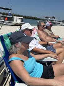 A group of friends relaxes on the beach, enjoying a sunny day by the water with fishing rods nearby — perfect for a laid-back fishing trip.