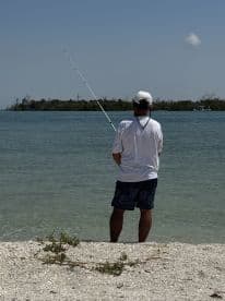 A man stands on the beach, fishing in tranquil waters, surrounded by a serene landscape — a perfect moment for fishing enthusiasts.
