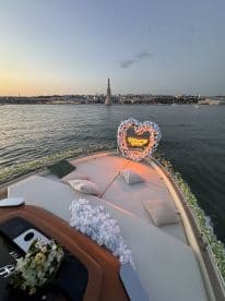 A beautifully decorated seating area on a boat, featuring floral arrangements and romantic lighting, perfect for proposals or special occasions on the water.
