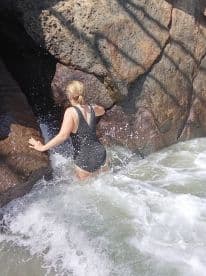 A woman navigates through the waves near rocky formations, showcasing the thrill of beach adventures and exploration.