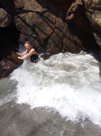 A woman enjoys a playful moment in the ocean waves at a rocky beach, capturing the thrill of swimming and adventure in nature.
