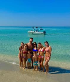 A joyful family poses together on the beach with a boat in the background, capturing a perfect day of fun in the sun and water activities.