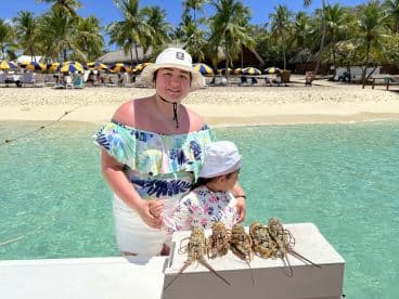 A joyful moment at the beach with a family, showcasing freshly caught lobsters against a picturesque backdrop of palm trees and beach umbrellas.