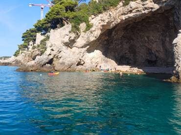 A vibrant scene of people kayaking and swimming near a stunning cave along the coastline, perfect for adventure seekers exploring the beauty of nature.