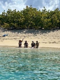A group of friends enjoys a sunny day at the beach, celebrating and relaxing in the shallow waters — a perfect sandbar stop for fun and laughter.