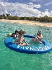 A group of friends enjoys a relaxing day in the water on a floating mat, sipping cocktails and soaking up the sun — the perfect beach getaway.