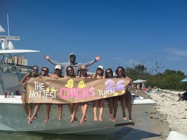 A lively group of friends celebrates a birthday on a boat, showcasing a fun banner while enjoying a sunny day at the beach.