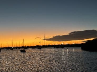 A stunning sunset casts vibrant colors over a harbor filled with boats, creating a picturesque scene perfect for evening cruises and relaxation by the water.