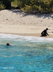 A child enjoys snorkeling in clear waters while an adult relaxes on the beach, showcasing a perfect day of fun and relaxation by the shore.