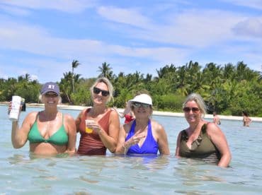 A group of friends enjoys a fun day swimming in shallow waters, celebrating with drinks and laughter against a tropical backdrop.