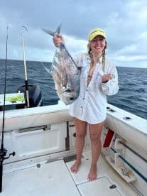 A joyful angler proudly displays her catch aboard a fishing boat, showcasing the thrill of a successful day on the water.