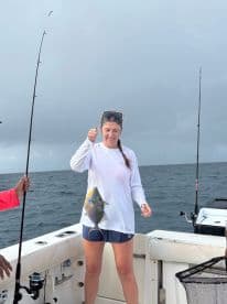A woman proudly displays her catch while fishing on a boat, showcasing the thrill of ocean adventures and the joy of reeling in a big one.