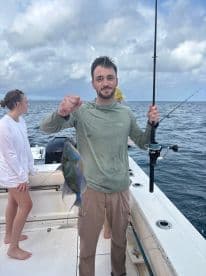 A young man proudly displays his catch while fishing on a boat, with friends enjoying the ocean experience — perfect for fishing trips and group adventures.