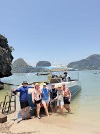 A cheerful group poses on the beach next to their boat, enjoying a sunny day out on the water — perfect for memorable adventures and celebrations.