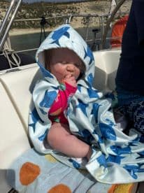 A cute baby wrapped in a shark-themed towel enjoys a sunny day on a boat, capturing the essence of family fun on the water.