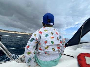 A child enjoys the scenic view from the deck of a boat, gazing out at the ocean and coastline — a perfect moment of adventure on the water.