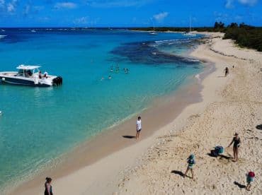 A vibrant beach scene featuring a group enjoying the clear waters and sandy shore, with a boat anchored nearby — perfect for family outings and fun in the sun.