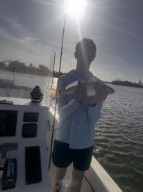 A young angler proudly displays his catch aboard a boat, basking in the sunshine — a perfect moment for fishing enthusiasts.