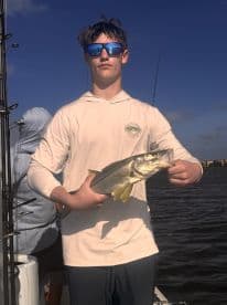 A young angler proudly displays his catch of a snook while fishing on a boat, capturing the thrill of a successful day on the water.