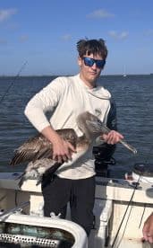 A young fisherman holds a pelican on a boat, showcasing a unique moment of human-animal interaction while enjoying a day out on the water.