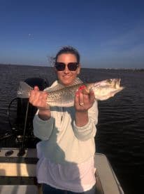 A woman proudly displays her catch while fishing on a boat, showcasing the thrill of outdoor fishing adventures.
