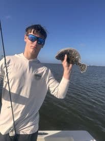 A teenager proudly holds up a flounder catch while fishing on a boat, showcasing the thrill of a successful day on the water.