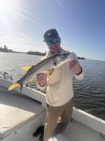 A man proudly displays his catch of a snook while fishing from a boat, showcasing the thrill of a successful day on the water.
