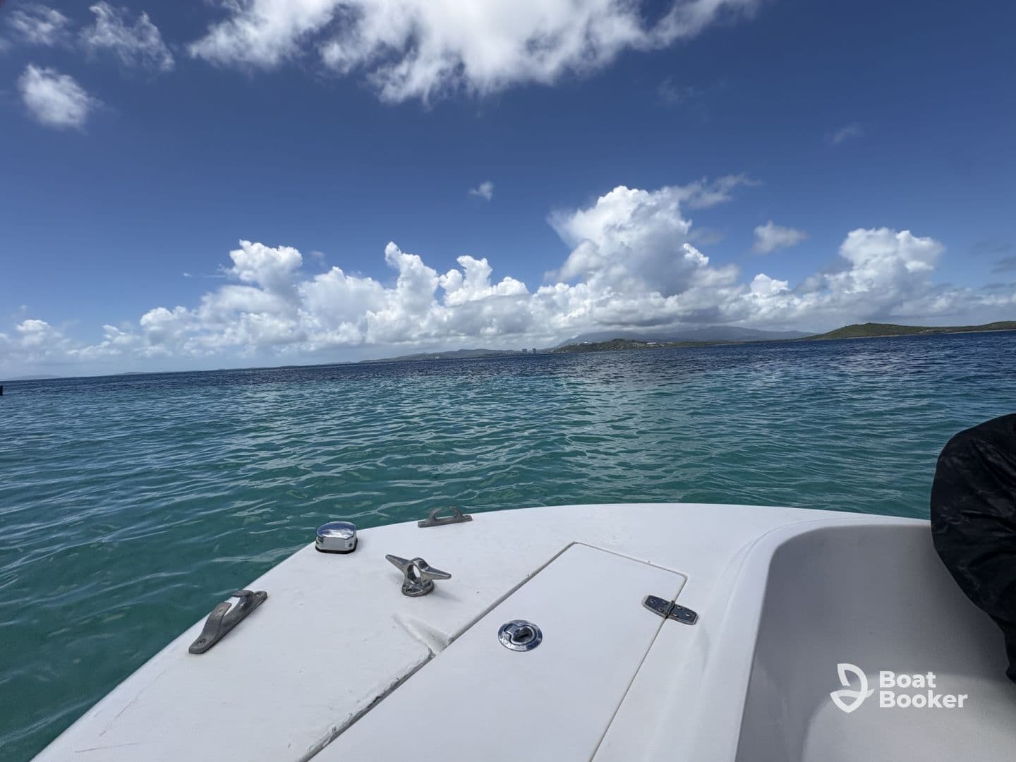 A serene view of a boat's bow cutting through clear turquoise waters, with a backdrop of fluffy clouds and distant islands — perfect for showcasing the beauty of a day on the water.