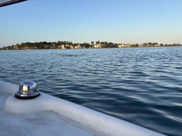 A serene view of the coastline from a boat, showcasing the tranquil waters and distant buildings, perfect for capturing the essence of a peaceful boating experience.