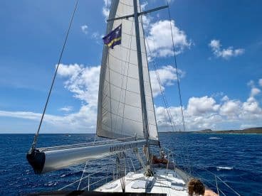 A scenic view from the deck of a sailboat, showcasing the vast ocean and blue skies, with guests enjoying the sailing experience.