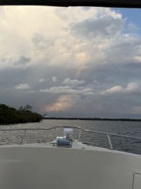 A serene view from the front of a boat, showcasing a rainbow amidst a cloudy sky — perfect for capturing the beauty of nature while on the water.