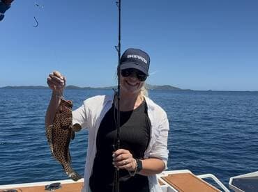 A joyful angler proudly displays her catch while fishing on a boat in the open ocean, showcasing the thrill of a successful day on the water.