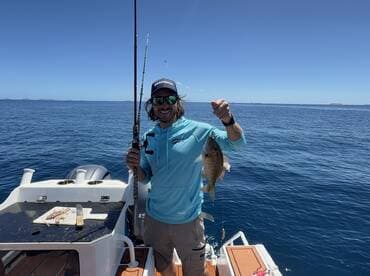 A man proudly displays his catch while fishing on a boat in clear blue waters — a perfect moment for fishing enthusiasts enjoying a day on the water.
